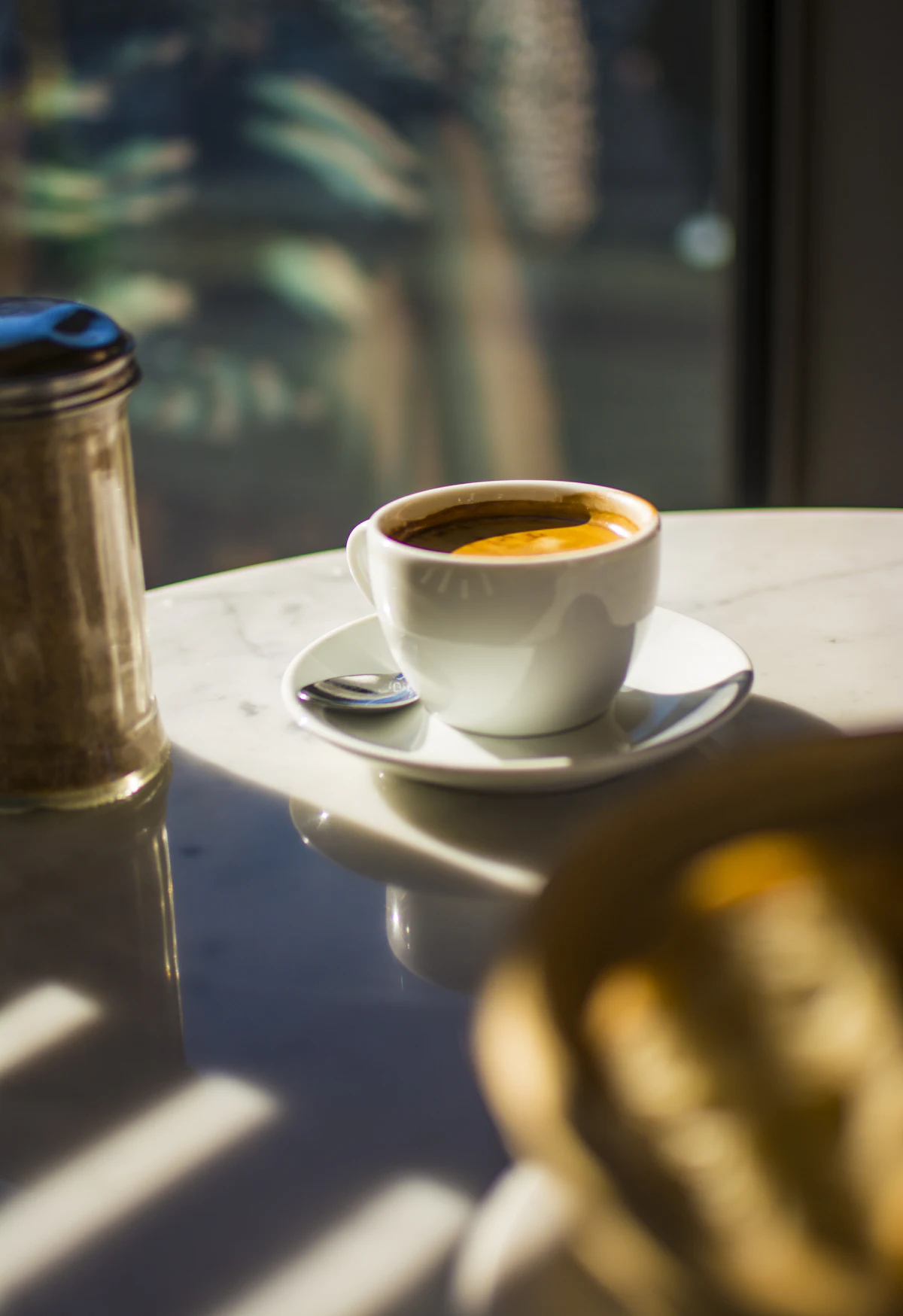 Taza de espresso humeante sobre una mesa de mármol iluminada por el sol de la mañana